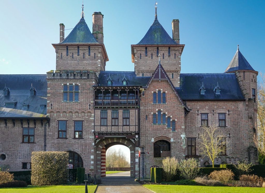 The original entrance building of De Haar Castle in the Netherlands, with a central arched gateway against a clear blue morning sky.